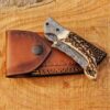Folded Damascus pocket knife resting on genuine leather sheath, anniversary gift.