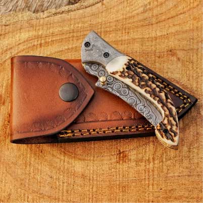 Folded Damascus pocket knife resting on genuine leather sheath, anniversary gift.