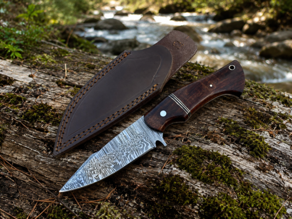 Custom Damascus hunting knife with leather sheath on forest ground