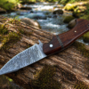 Damascus steel skinner knife placed on rock beside river outdoors