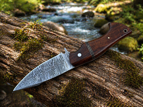 Damascus steel skinner knife placed on rock beside river outdoors