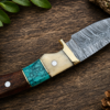 Handmade Damascus hunting knife displayed on wooden surface with greenery