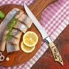 Handmade fillet knife cutting fresh fish with lemon and herbs.