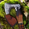 Close-up of engraved Norse Viking axe blade with wooden handle and leather sheath