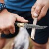 Handmade Damascus folding knife carving wood during outdoor camping activity.
