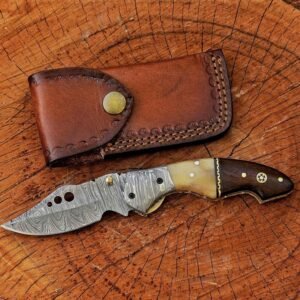 Damascus folding pocket knife with camel bone and rosewood handle beside leather sheath