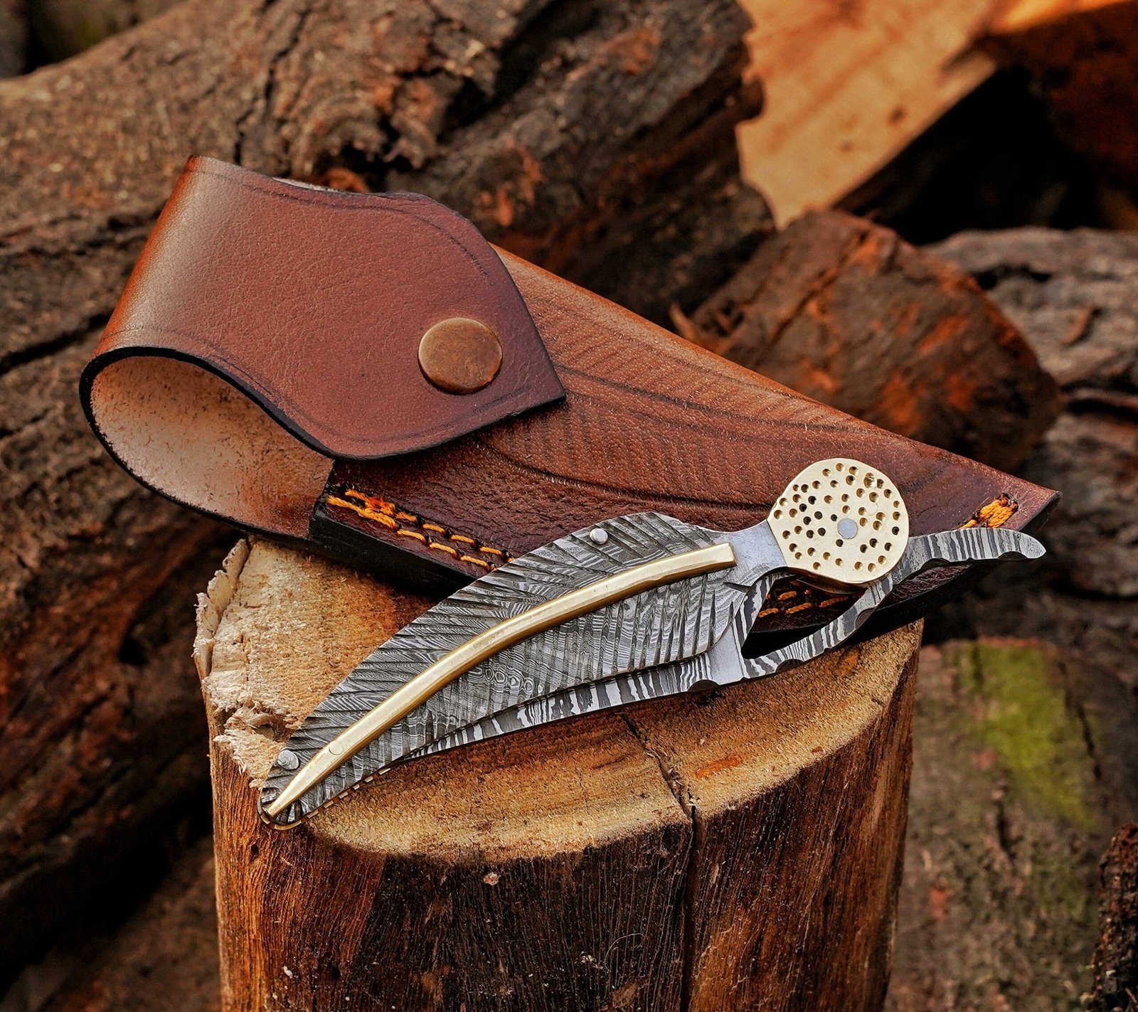 Damascus steel folding knife displayed over a brown leather sheath
