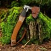 Viking-style handmade axe with leather-wrapped handle and decorative engraved head displayed on a moss-covered tree stump